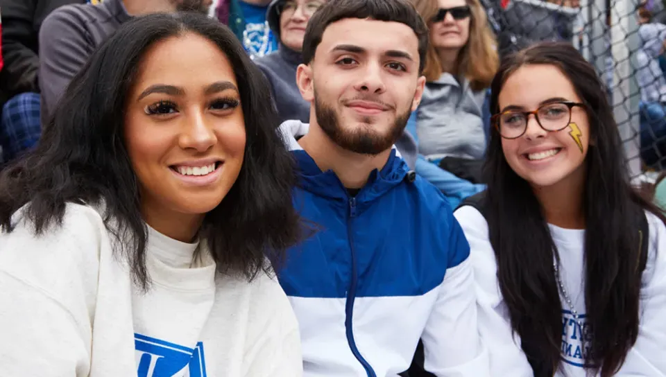 Three U N E students at a U N E football game